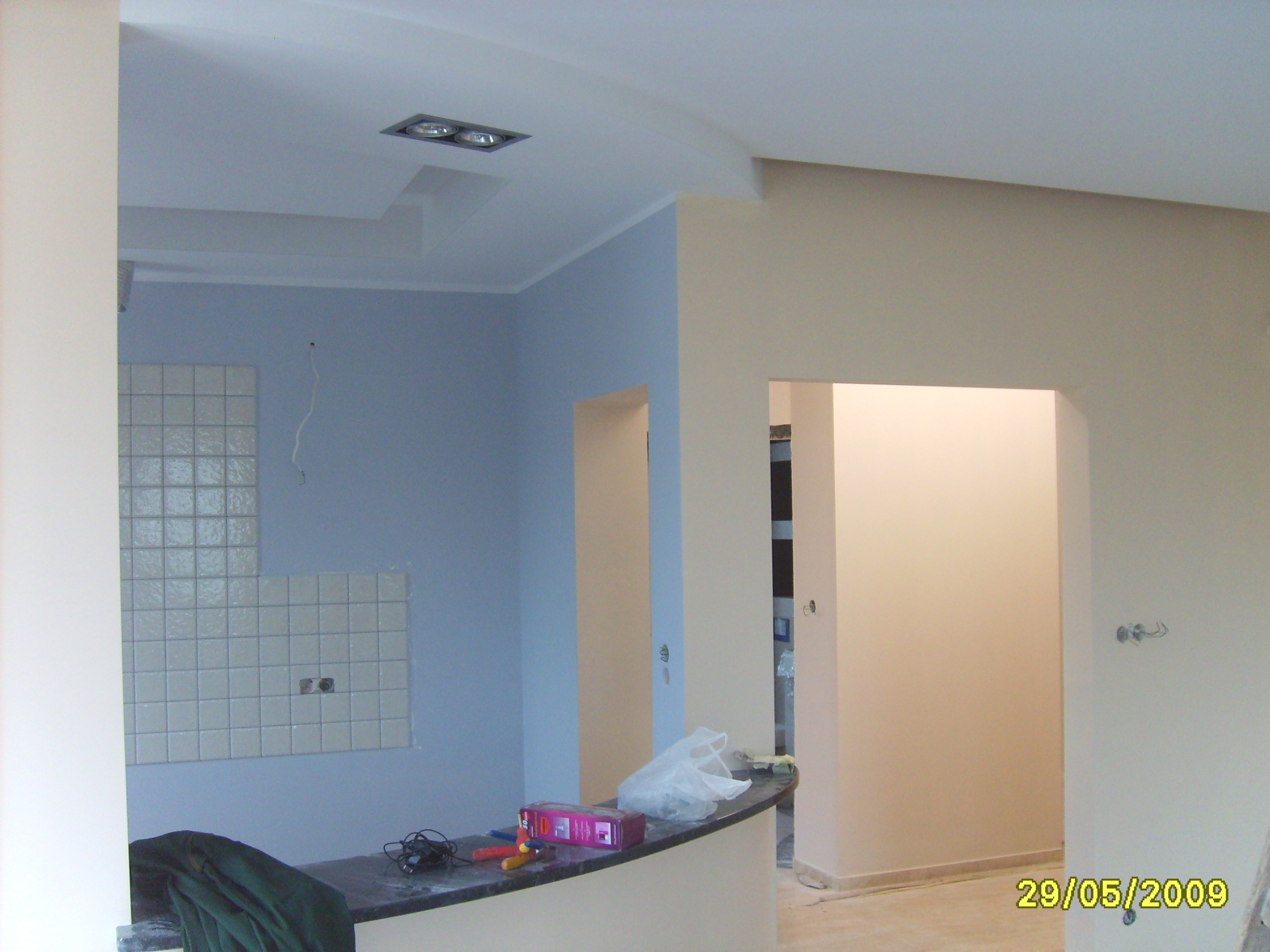 Wnętrze w trakcie prac wykończeniowych, widoczne fragmenty ścian pomalowanych na niebiesko i beżowo, częściowo ułożona mozaika z płytek oraz narzędzia na blacie.